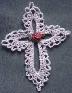 a crocheted white cross with a red rose on the center is laying on a gray surface