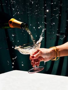 a person pouring champagne into a wine glass with confetti falling from the top