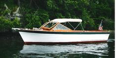 a white and brown boat floating on top of a lake next to lush green trees