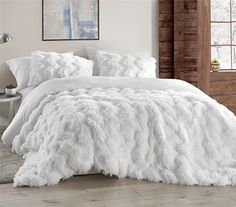 a bed with white comforter and pillows in a room next to a brick wall