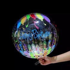 a person holding a large balloon with the words happy birthday written on it, in front of a black background