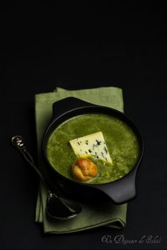 a black bowl filled with green soup and cheese