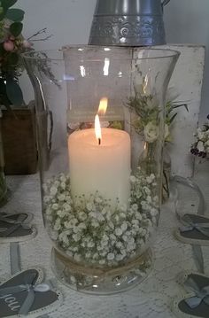 a lit candle sitting inside of a glass vase filled with flowers and greenery on top of a table