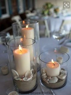 two clear vases filled with sand and lit candles on top of a white table cloth