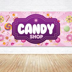 a candy shop sign hanging on the wall next to a wooden floor in front of a white brick wall