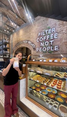 a woman standing in front of a bakery counter holding a bag of coffee and looking at the camera