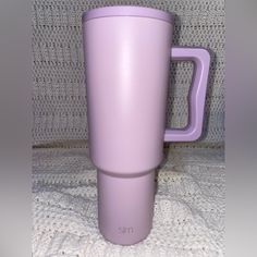 a purple coffee cup sitting on top of a white blanket next to a gray wall