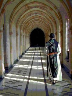 a person walking down a long hallway with an archway on one side and tiled floors on the other