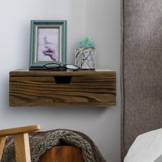 a wooden shelf sitting above a bed next to a chair and framed photo on the wall