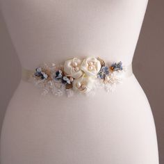 Gold blue  wedding sash Bridesmaid belt Color: gold /ivory/dusky blue with grey accent flowers  Materials:ivory lace , handmade  fabric flowers,blue paper flowers, beads,gold metal leaves, freshwater and faux pearls,wire,satin ribbon. Measurements: Applique approx L 7 inches, W 2.5 inches Applique attached to  ivory satin ribbon 25mm x 260 cm. MORE SASHES: https://www.etsy.com/uk/shop/WeddingJewelryOutlet?ref=seller-platform-mcnav§ion_id=26791561 WEDDING JEWELRY: https://www.etsy.com/uk/shop/WeddingJewelryOutlet?ref=seller-platform-mcnav§ion_id=26786154   MATCHING HEADPIECES: https://www.etsy.com/uk/shop/WeddingJewelryOutlet?ref=simple-shop-header-name&listing_id=724957245§ion_id=26785826 *Please NOTE colors may be slightly different than the monitor shows due to monitor differences. Some Elegant Blue Sashes For Wedding, Elegant Blue Bridal Belt For Wedding, Elegant Bridal Belt With Flower Decoration For Wedding, Adjustable Bridal Belt With Sashes For Bridesmaid, Adjustable Bridesmaid Bridal Belt With Sashes, Elegant Bridal Belt With Handmade Flowers For Weddings, Gold Bridal Dress, Sash Wedding Dress, Bridesmaid Belt