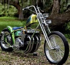 a green and black motorcycle parked on top of a grass covered field with trees in the background