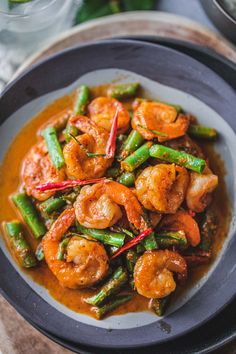 shrimp and asparagus stir - fry with sauce in a black bowl on a wooden table