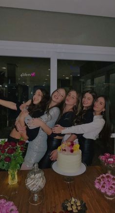 a group of women standing next to each other in front of a cake on top of a table