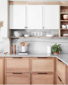 a white kitchen with wooden cabinets and marble counter tops, along with potted plants