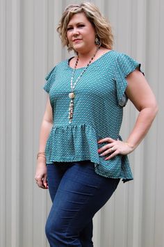 a woman standing in front of a wall wearing jeans and a top with ruffles