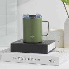 a green coffee mug sitting on top of a stack of books next to a plant