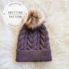 a knitted hat with a pom - pom sits on top of a fluffy white blanket