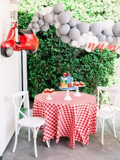 a red scooter is hanging from the side of a wall next to a table covered in balloons