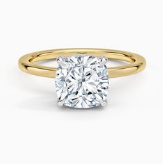 a yellow gold ring with a cushion cut diamond in the center, on a white background