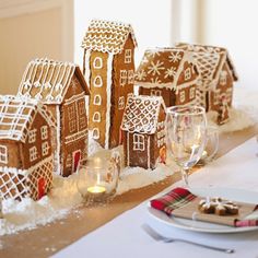 gingerbread houses are displayed on a table with wine glasses and plates in front of them