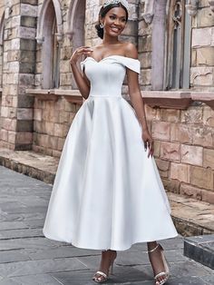 a woman wearing a white dress standing in front of a stone building with her hands on her hips