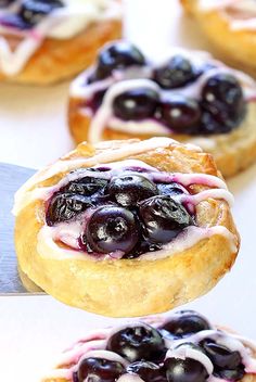 blueberry danish pastries with icing on a white surface next to a knife