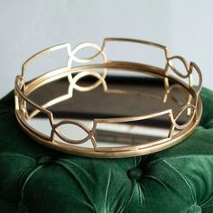 a green velvet ottoman with a gold metal tray on it's back and an oval mirror in the middle