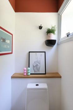 a white toilet sitting under a window next to a wooden shelf filled with candles and potted plants