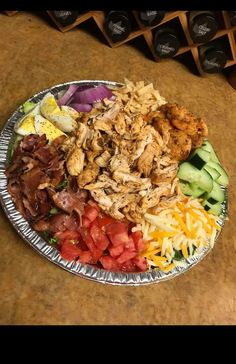 a metal plate filled with lots of food on top of a wooden table next to wine bottles