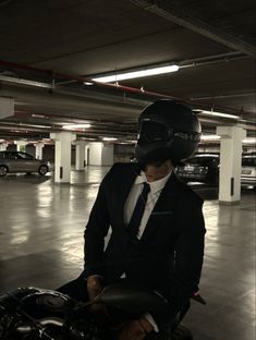 a man wearing a suit and tie sitting on a motorcycle in a parking garage next to parked cars