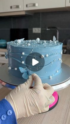 a person in gloves is decorating a cake with blue icing and white pearls