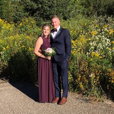 a man and woman standing next to each other in front of wildflowers on a sunny day