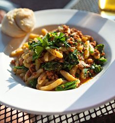 a white plate topped with pasta and veggies next to a glass of beer