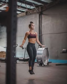 a woman standing in a gym holding a skipping rope and looking up at the sky