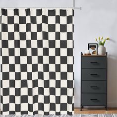 a black and white checkered shower curtain next to a dresser with a potted plant