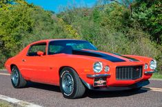 an orange muscle car parked on the side of the road in front of some trees