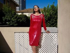 a woman in a red dress leaning against a fence with her hands on her hips