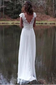 a woman standing in front of a lake wearing a white dress