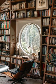 a room filled with lots of books and a round window in the wall next to a chair