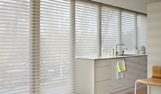 a kitchen area with a sink, counter and window coverings in shades of white