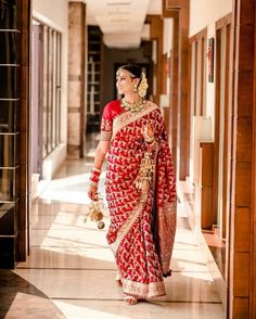 a woman in a red and gold sari walking down the hall with her hand on her hip