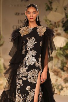 Black gown with sequin embellished floral motifs. Comes with ruffle cape embellished by feather and floral applique.
Components: 2
Pattern: Embroidered
Type Of Work: Sequin
Neckline: Gown: Round, Cape: Open
Sleeve Type: Cape: Cape sleeves
Fabric: Crepe, Georgette and Tulle
Color: Black
Other Details: 
Length:
Gown: 60 inches
Cape: 75 inches
Note: Jewellery worn by the model is not for sale
Occasion: Cocktail,Reception - Aza Fashions Embellished Pre-draped Saree With Cape Sleeves For Evening, Evening Pre-draped Saree With Resham Embroidery And Cape Sleeves, Embellished Choli With Cape Sleeves, Festive Gown With Hand-embellished Cape Sleeves, Festive Hand-embellished Gown With Cape Sleeves, Gown Cape, Varun Bahl, Cape For Women, Crepe Gown