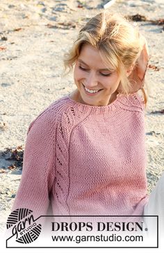 a woman sitting on the ground wearing a pink sweater