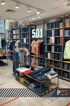 Interior da loja da marca de roupas Levi’s, no Shopping Riomar, em Recife. Araras dispostas junto as paredes e distribuídas pelo salão da loja apresentam os produtos da marca, a maioria em tecido jeans, alguns pendurados em cabides e outros dobrados em estantes. Os móveis de apoio, caixa, portas do provador são todos em madeira e com toques industriais. Todo o ambiente é muito bem iluminado. Men's Clothing Store Design, Clothing Shop Interiors, Clothing Store Interior Design, Fashion Shop Interior, Retail Store Layout, Shop Counter Design, Fashion Store Design, Store Shelves Design, Retail Store Interior Design