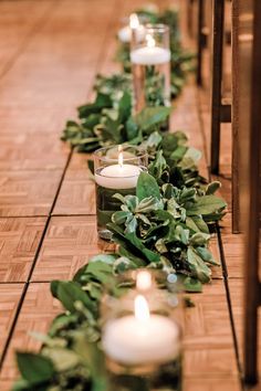 candles are lined up on the floor with greenery