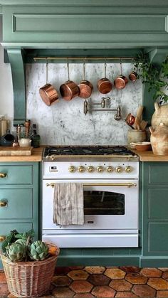 a kitchen with green cabinets and pots on the wall above an oven, pot rack holding utensils