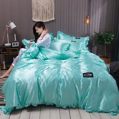 a woman sitting on the floor in front of a bed with blue sheets and pillows