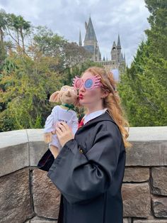 a woman in graduation gown holding a teddy bear and wearing goggles on top of a stone wall