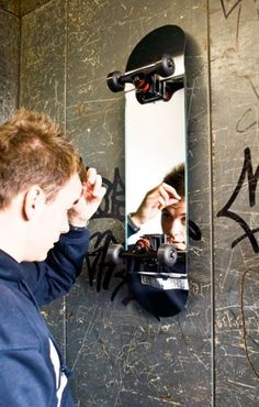 a man looking at himself in the mirror with graffiti on the wall behind him,