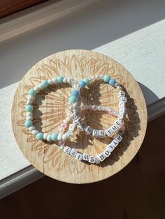 three bracelets with words on them sitting on top of a wooden plate in front of a window